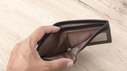 Close up of hand opens an empty wallet on wooden background.